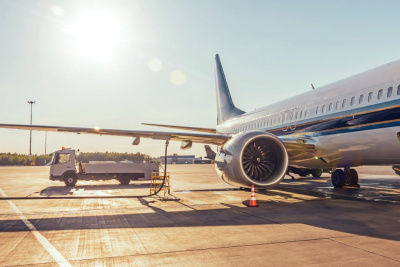 Ein Passagierflugzeug auf einem Flughafen, das bei hellem Sonnenlicht und blauem Himmel von einem Tankwagen betankt wird.