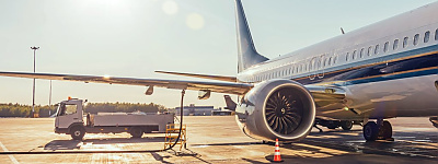 InnoFuels Projektbild Ein Passagierflugzeug auf einem Flughafen, das bei hellem Sonnenlicht und blauem Himmel von einem Tankwagen betankt wird.