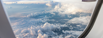 CENA SAF-Outlook Aufnahme aus einem Flugzeugfenster mit Blick auf einen Flugzeugflügel und auf den blauen Himmel mit Wolken.